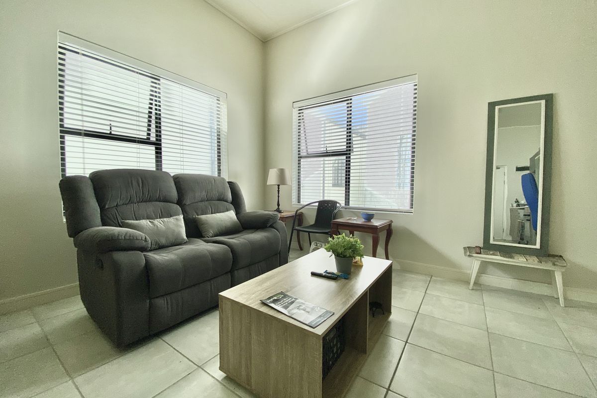 A bright living room featuring large windows with venetian blinds and neutral tiled flooring, offering a clean and functional space.