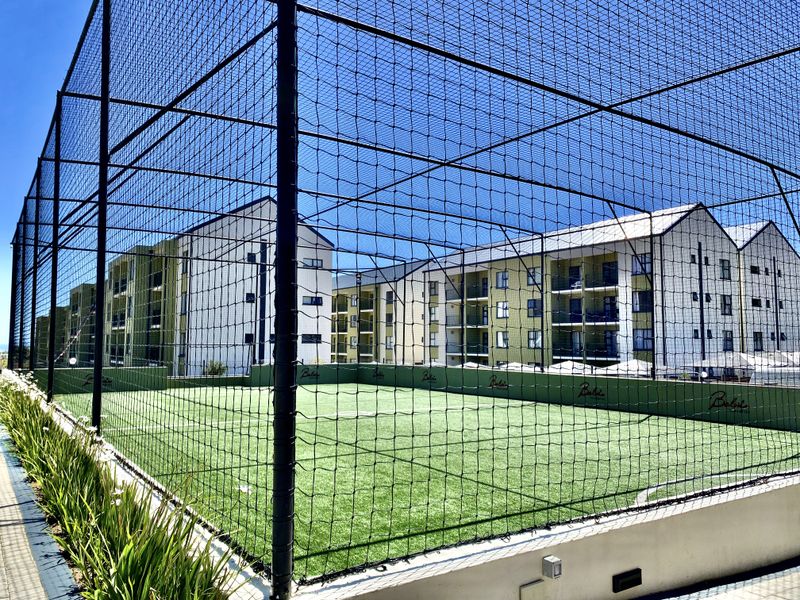 A well-maintained outdoor sports facility featuring artificial turf and secure perimeter netting, situated within a modern apartment complex.