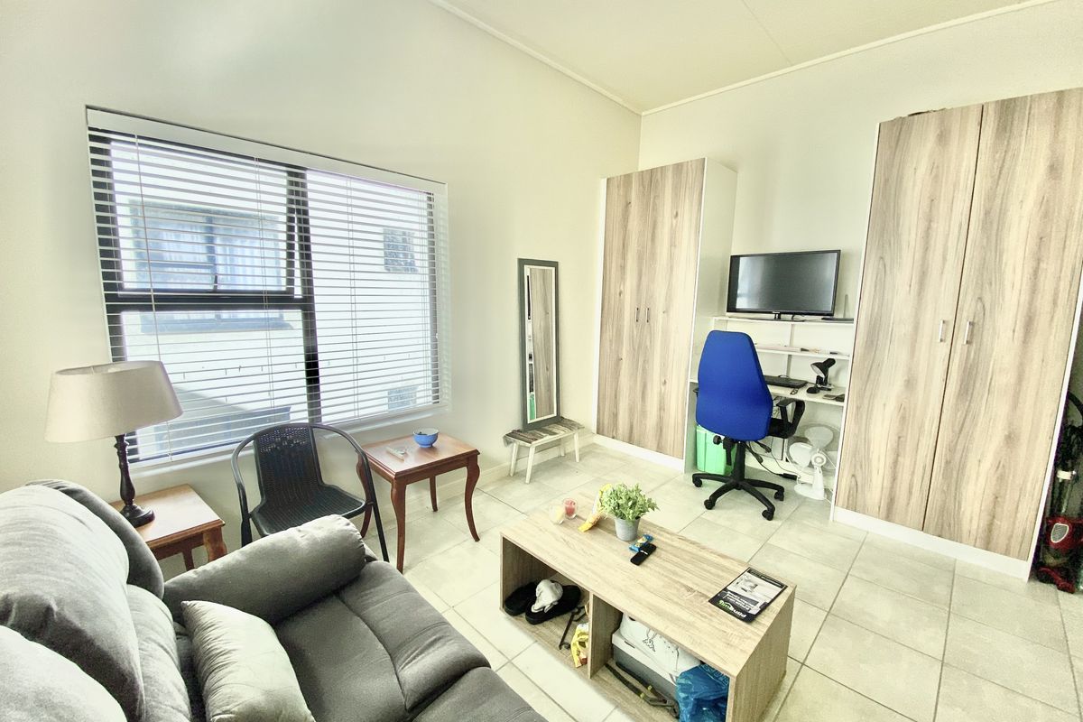 A functional bedroom featuring built-in cupboards, tiled flooring, and large windows with venetian blinds, offering a practical living space.