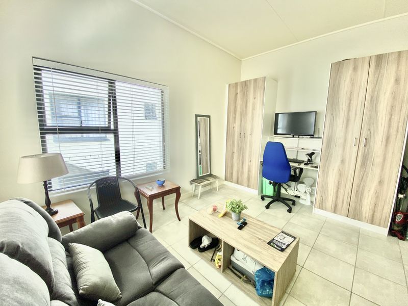 A functional bedroom featuring built-in cupboards, tiled flooring, and large windows with venetian blinds, offering a practical living space.