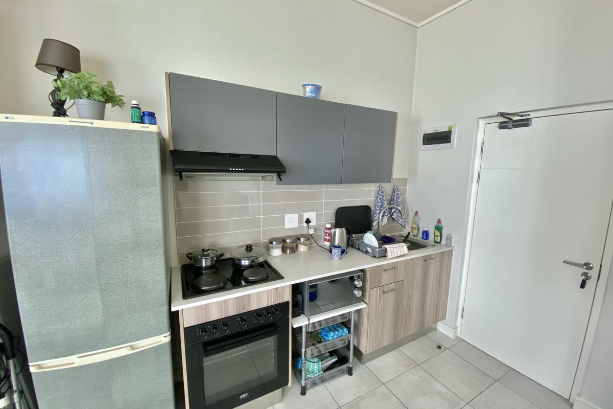Compact kitchen featuring modern grey and wood-tone cabinetry, built-in oven with hob, extractor fan, and tiled backsplash with neutral floor tiles.