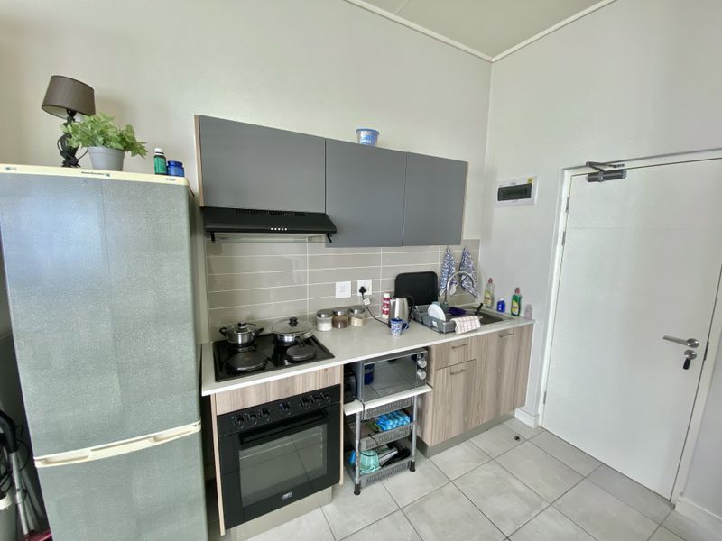Compact kitchen featuring modern grey and wood-tone cabinetry, built-in oven with hob, extractor fan, and tiled backsplash with neutral floor tiles.