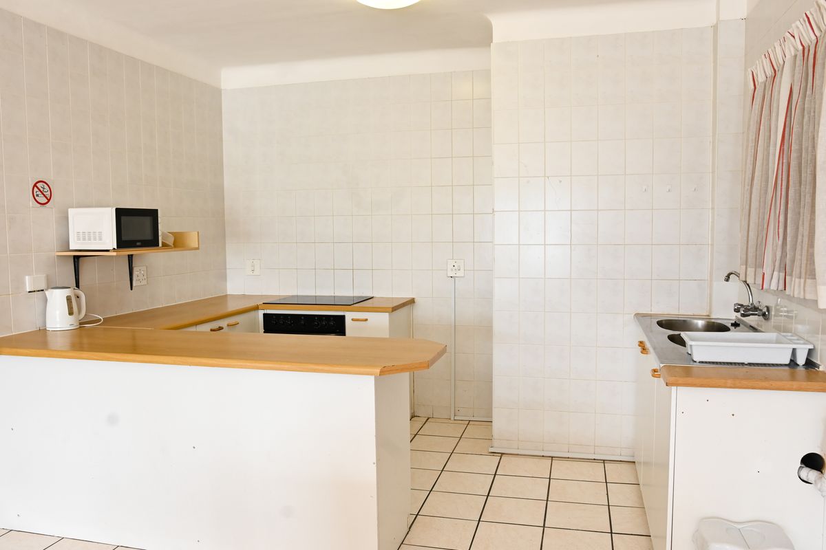 A dated, empty kitchen featuring white tiled walls, ceramic floor tiles, laminate countertops, and basic built-in cabinetry with an integrated electric hob and oven.