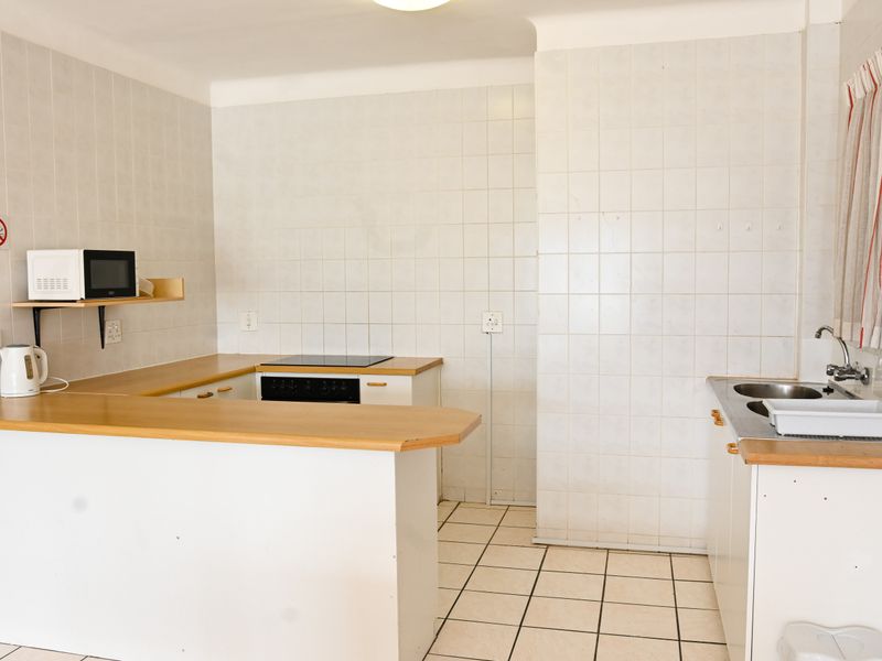 A dated, empty kitchen featuring white tiled walls, ceramic floor tiles, laminate countertops, and basic built-in cabinetry with an integrated electric hob and oven.