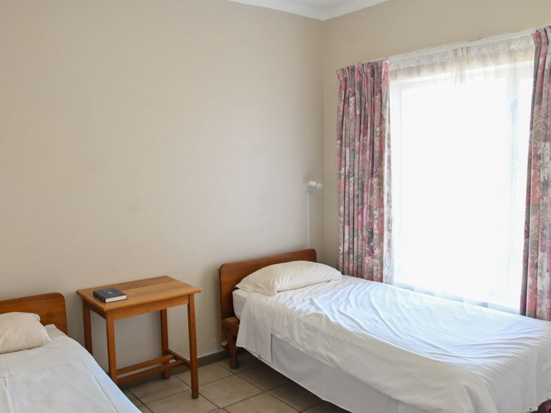 A functional bedroom featuring tiled flooring and a large window with curtain tracks, providing natural light.