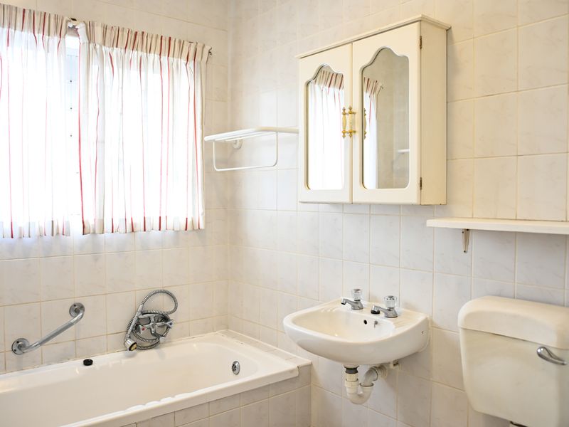 A dated bathroom featuring a bathtub, wall-mounted basin, and toilet cistern with full-height wall tiling and a built-in medicine cabinet.