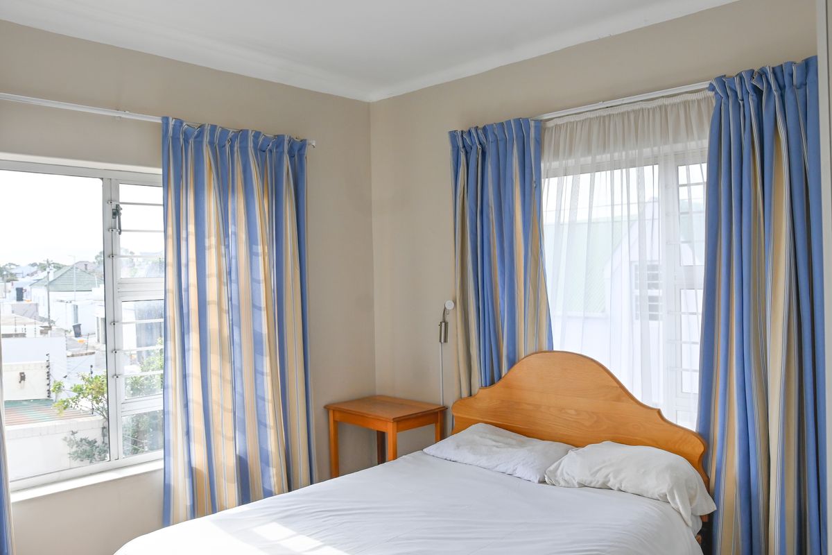 A bright bedroom featuring neutral walls, coving, and dual windows with aluminium frames, offering natural light and a view of the surrounding neighbourhood.