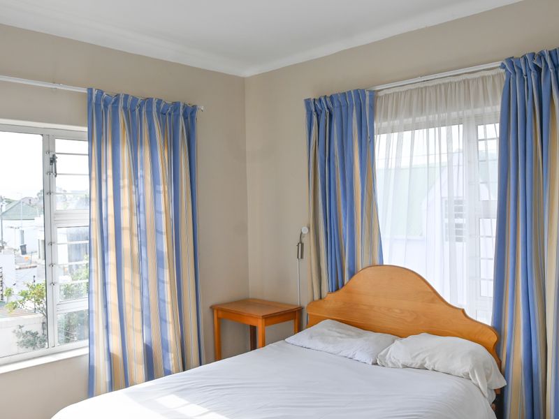 A bright bedroom featuring neutral walls, coving, and dual windows with aluminium frames, offering natural light and a view of the surrounding neighbourhood.