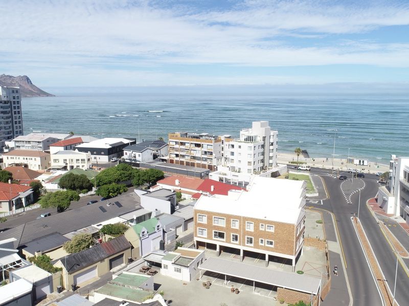 An aerial view of the coastal apartment complex and surrounding urban neighborhood, showcasing proximity to the beach and local infrastructure.
