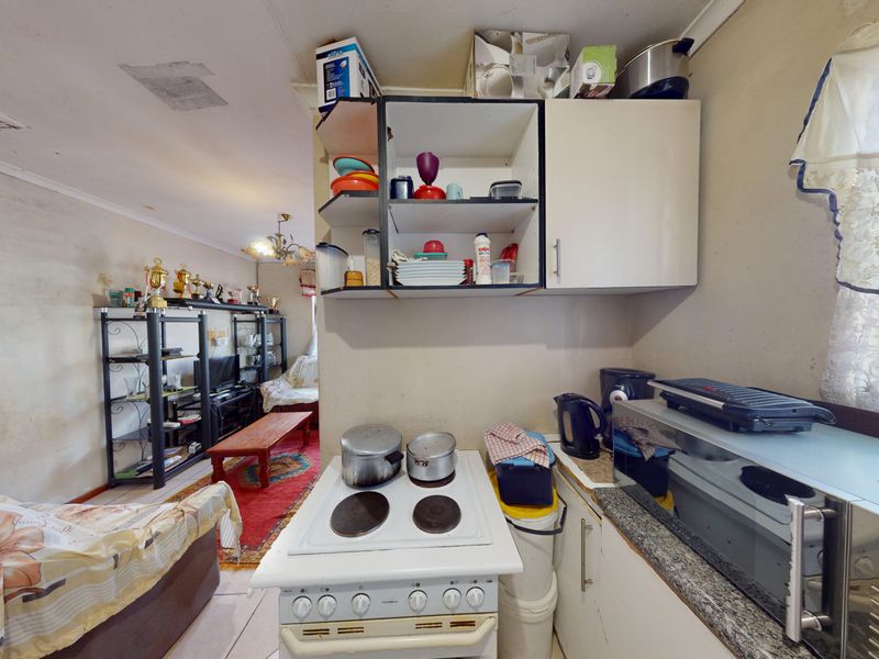 Open-plan living and kitchen area featuring basic cabinetry, electric stove, and granite countertops, requiring cosmetic updates and wall repairs.
