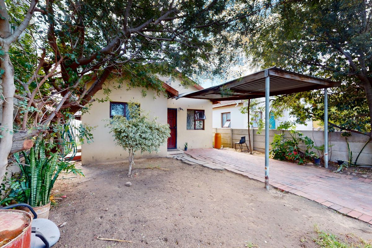 Rear exterior view of the house featuring a paved driveway, a metal carport structure, and a perimeter boundary wall.