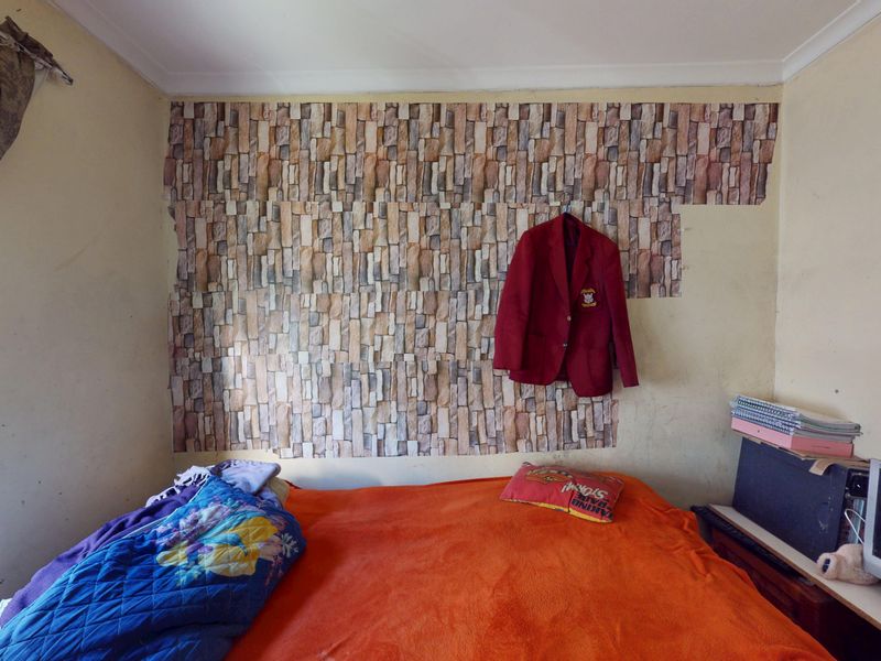 A bedroom featuring a decorative stone-effect wallpaper accent wall and a window with coving detail.