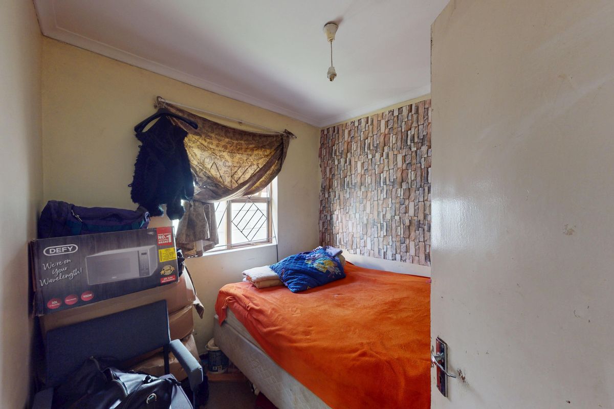 A compact bedroom featuring a window with security bars and a feature wall with stone-effect wallpaper.