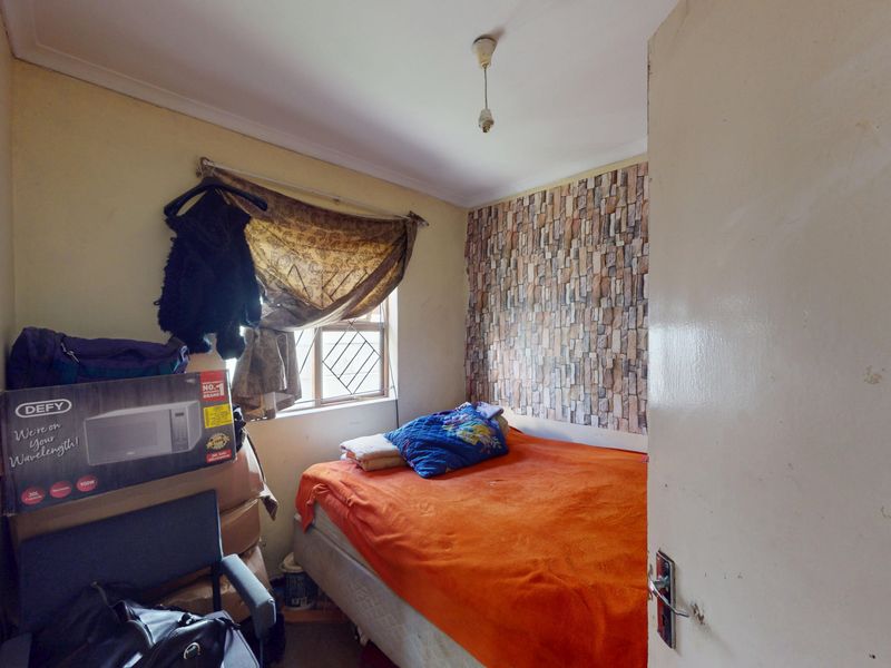 A compact bedroom featuring a window with security bars and a feature wall with stone-effect wallpaper.