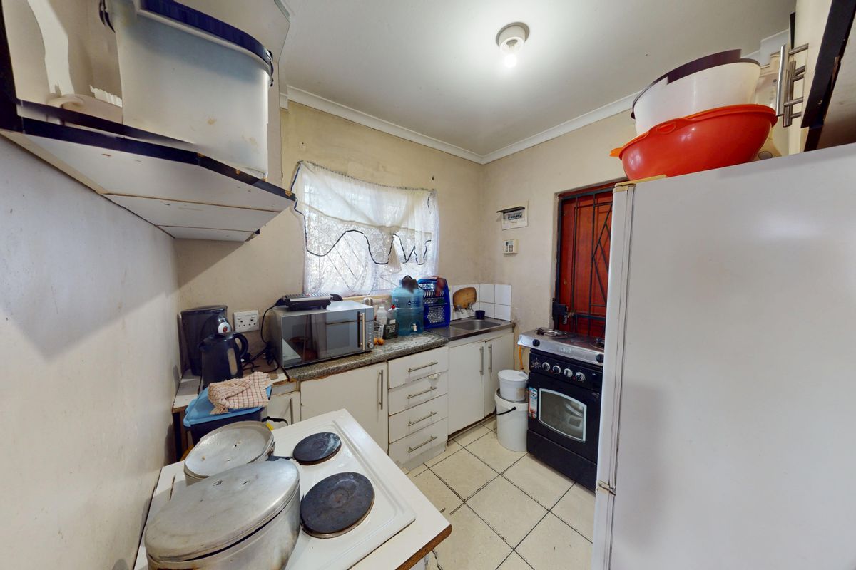 A compact kitchen featuring tiled flooring, built-in cabinetry, a stainless steel sink, and a freestanding oven with a security gate at the rear entrance.
