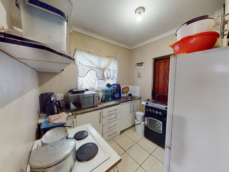 A compact kitchen featuring tiled flooring, built-in cabinetry, a stainless steel sink, and a freestanding oven with a security gate at the rear entrance.