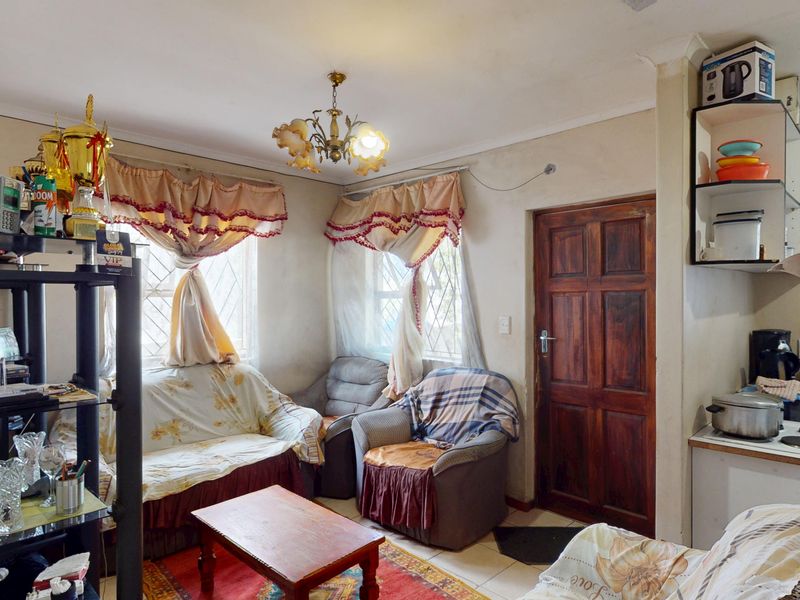 A living room area featuring tiled flooring, a wooden door, and diamond-patterned window panes, requiring cosmetic updates to improve the overall aesthetic.
