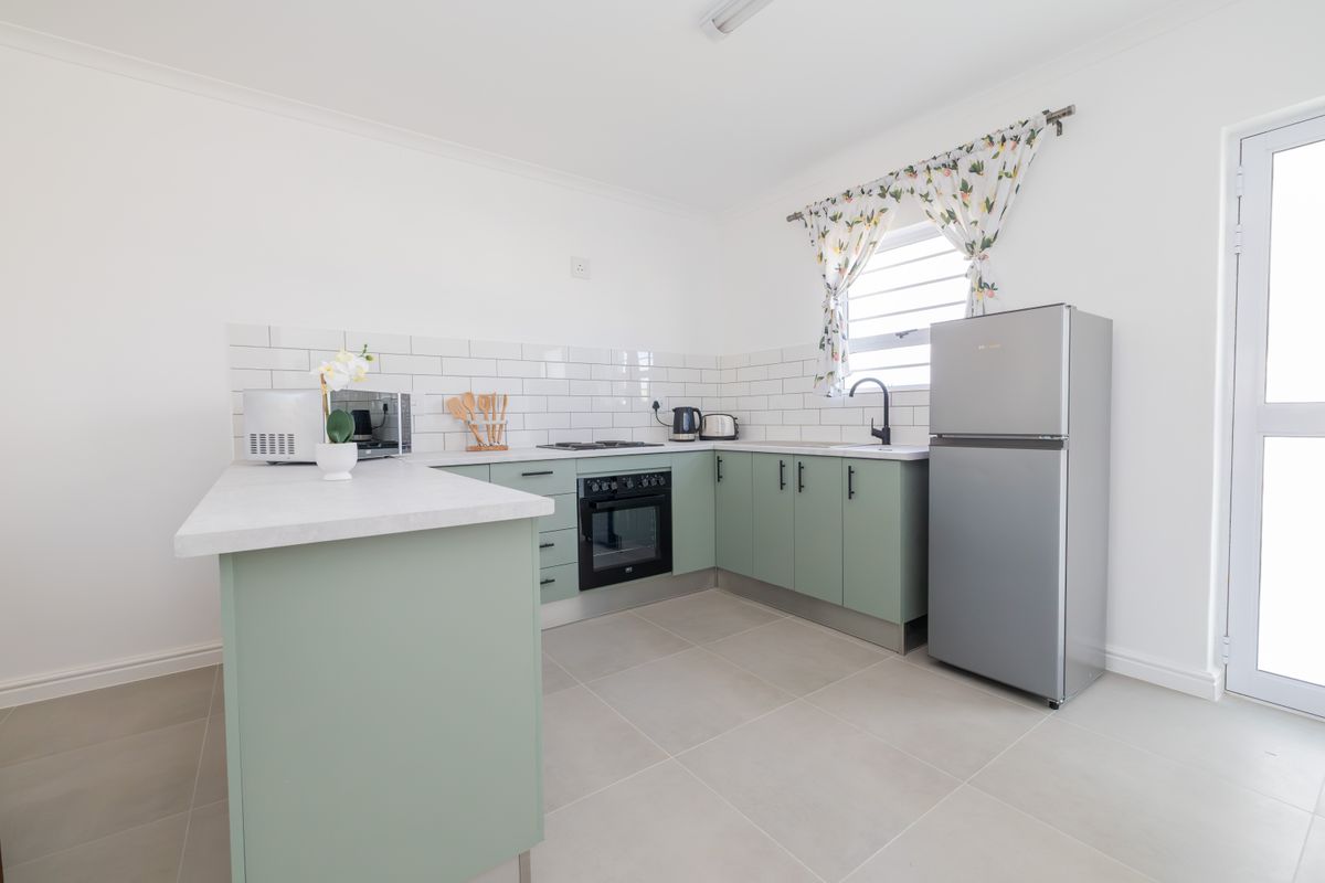 A modern, well-maintained kitchen featuring sage green cabinetry, white subway tile backsplash, built-in oven, hob, and neutral tiled flooring.