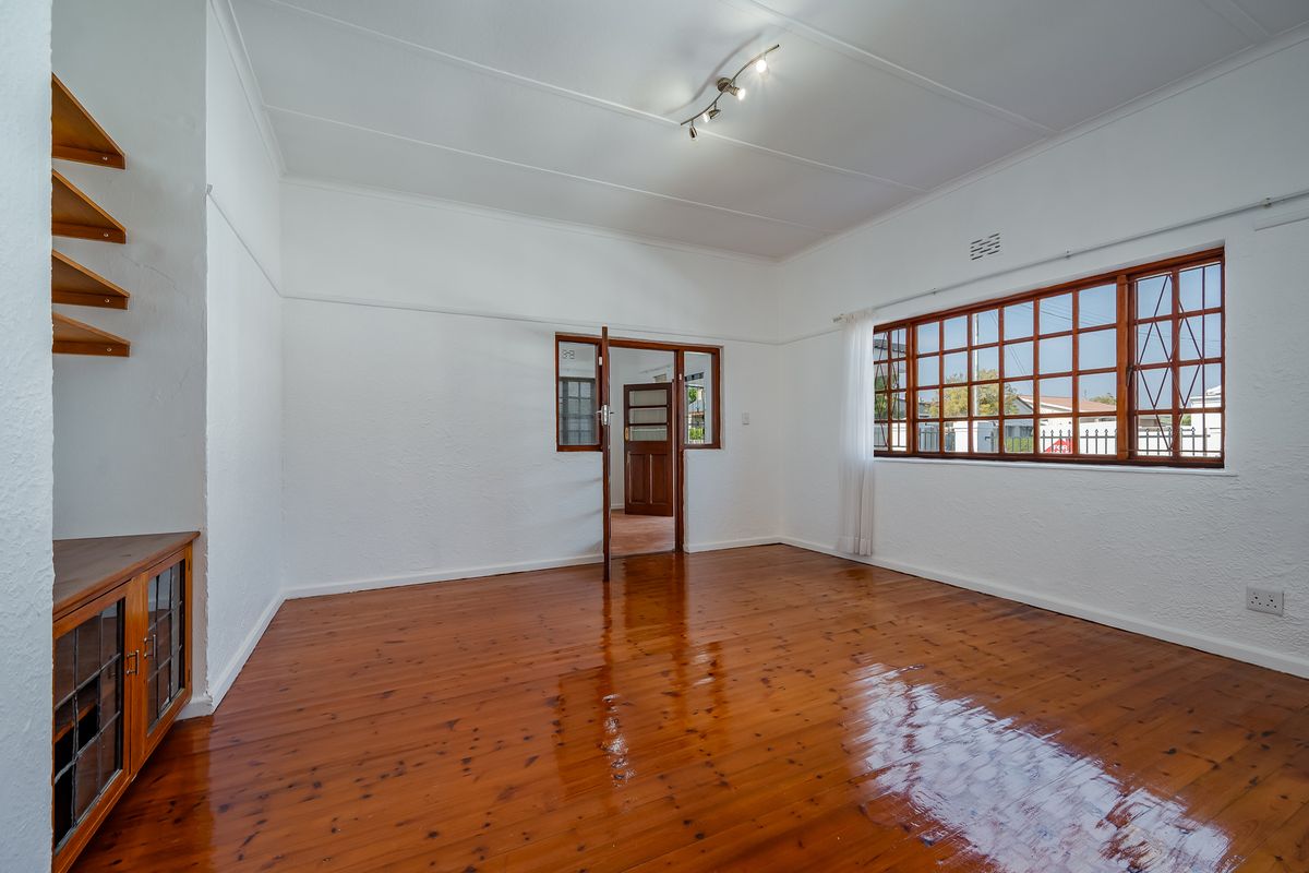 A bright and spacious living room featuring polished hardwood flooring, built-in wooden cabinetry, and classic timber-framed windows.