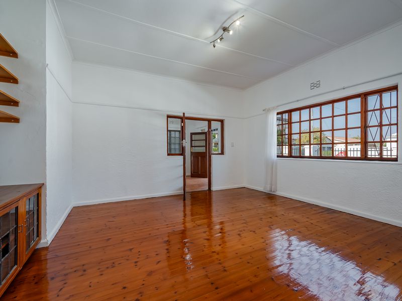 A bright and spacious living room featuring polished hardwood flooring, built-in wooden cabinetry, and classic timber-framed windows.