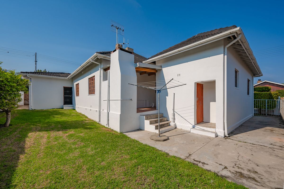 Rear view of the house featuring a white facade, tiled roof, concrete patio area, and a small garden space.