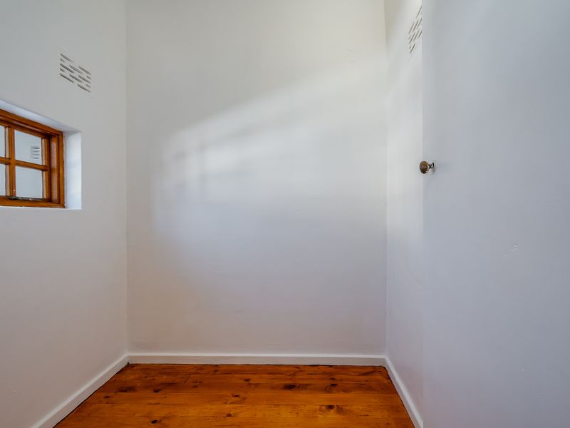 A small, empty room featuring polished timber flooring, a timber-framed window, and white walls, suitable for a variety of uses.