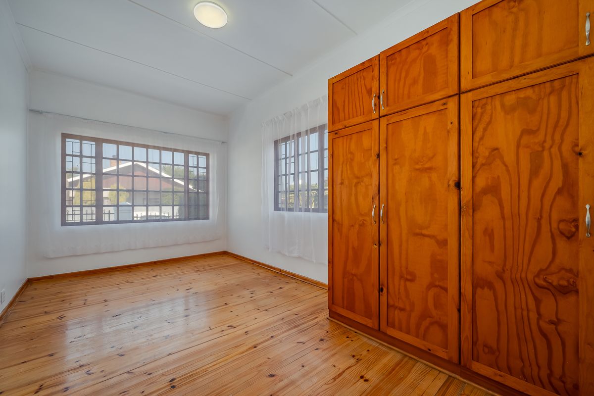 A bright, empty bedroom featuring polished wooden flooring, large grid-pattern windows, and extensive built-in wooden cabinetry.