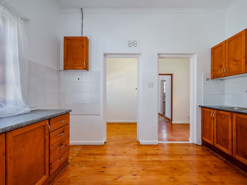A functional kitchen featuring timber cabinetry, laminate countertops, a stainless steel sink, and warm timber flooring, offering a classic aesthetic ready for modernization.