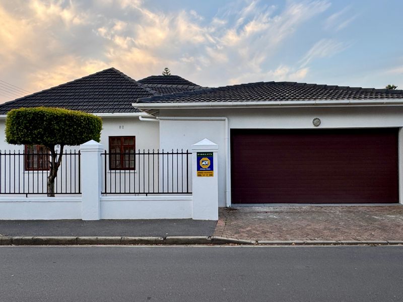 Front elevation of a well-maintained house featuring a tiled roof, secure wrought iron fencing, and a double garage with a paved driveway.