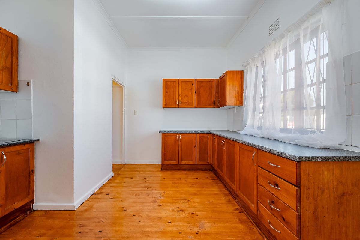 A functional kitchen featuring timber cabinetry, laminate countertops, and polished wooden flooring, offering a clean and well-maintained space ready for updates.