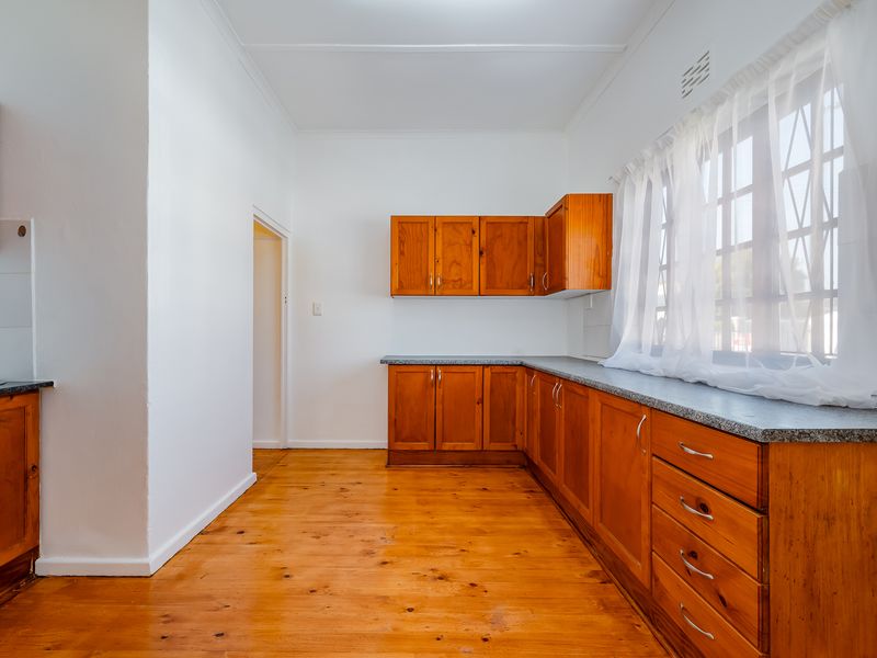 A functional kitchen featuring timber cabinetry, laminate countertops, and polished wooden flooring, offering a clean and well-maintained space ready for updates.