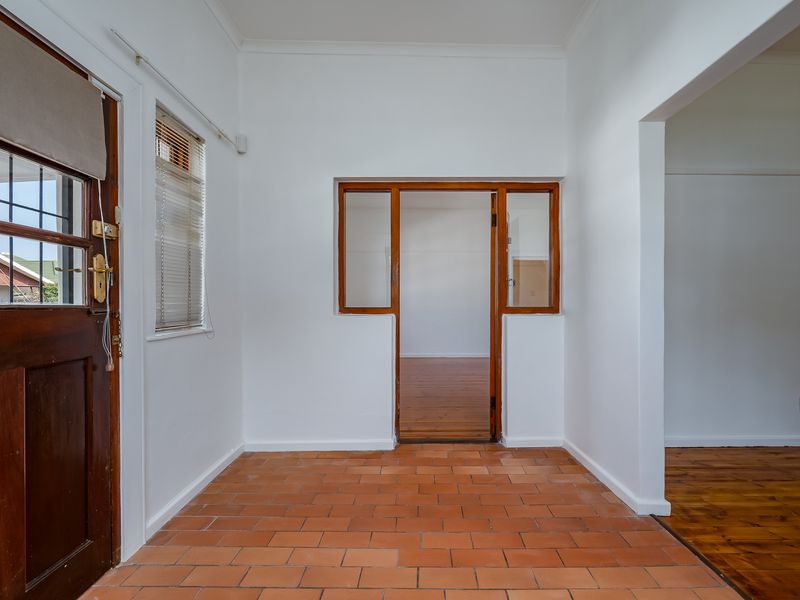 A bright, empty entrance hall featuring terracotta tile flooring, a timber door frame, and a view into the adjacent living area with timber floors.
