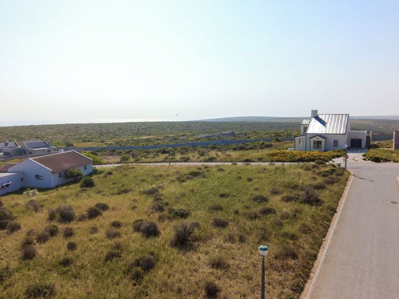 An aerial view of a residential area featuring paved roads, street lighting, and surrounding coastal landscape with existing residential properties.