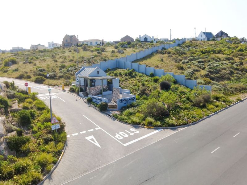 Aerial view of the Hoogland Estate entrance, featuring a security gatehouse, perimeter walling, and paved access roads within a landscaped residential setting.