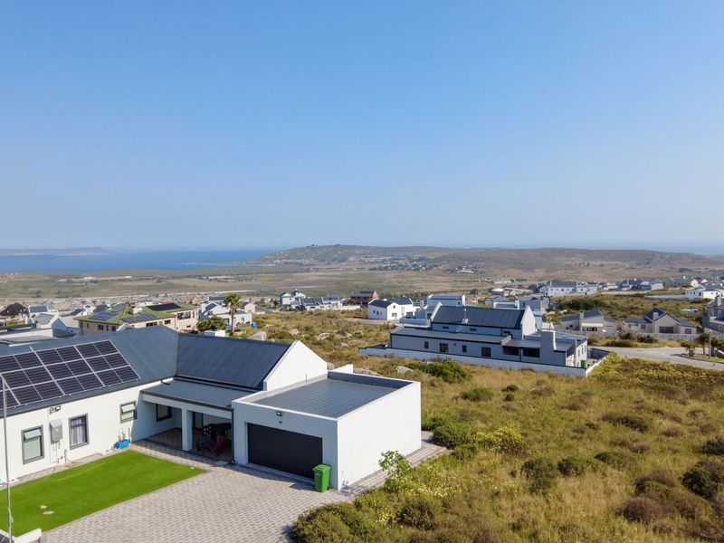 Aerial view of a modern residential property featuring a paved driveway, garage, solar panels, and a well-maintained lawn in a coastal estate setting.