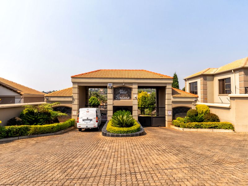 The main entrance to Villa Fontana townhouse complex, featuring a paved driveway, secure gated access, and well-maintained perimeter walls and landscaping.