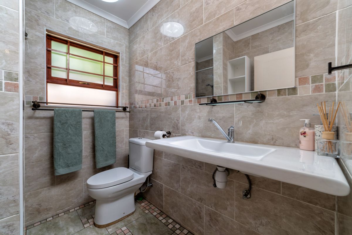 A well-maintained bathroom featuring floor-to-ceiling neutral tiling, a wall-mounted basin, and a functional toilet with a window for natural light.