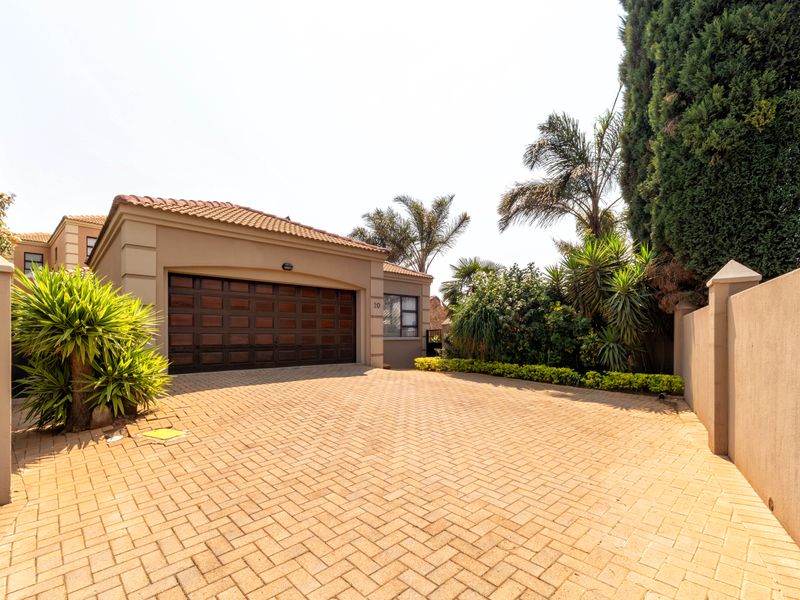 Front exterior view of the townhouse featuring a paved driveway, double garage, and well-maintained boundary walls with established landscaping.