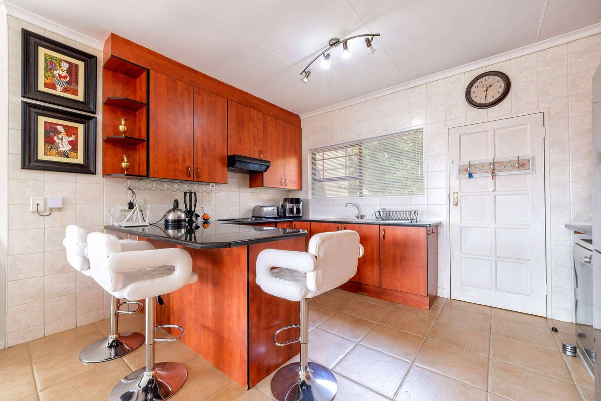 A functional kitchen featuring warm-toned wooden cabinetry, granite countertops, a breakfast bar, and tiled finishes throughout.