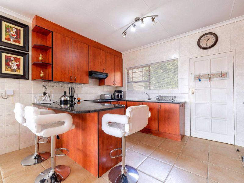 A functional kitchen featuring warm-toned wooden cabinetry, granite countertops, a breakfast bar, and tiled finishes throughout.