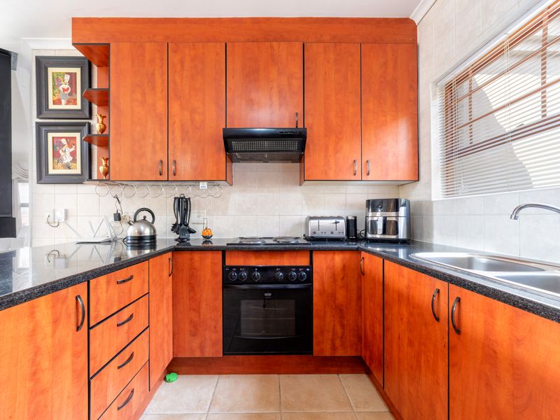 A functional U-shaped kitchen featuring warm-toned laminate cabinetry, granite countertops, a built-in oven with hob, and a stainless steel double sink.