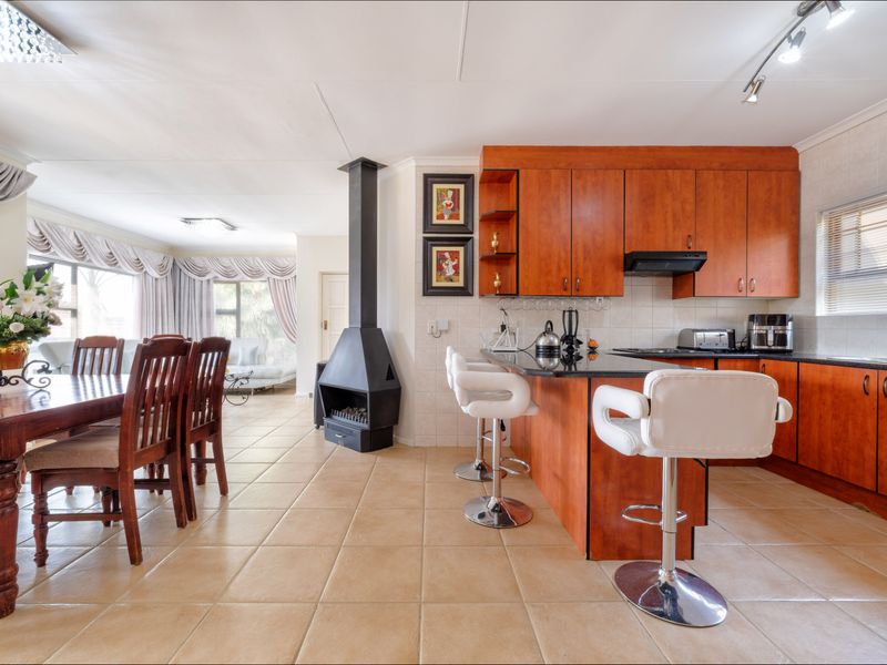 Open-plan living and kitchen area featuring a central wood-burning fireplace, wooden cabinetry, granite countertops, and tiled flooring throughout.