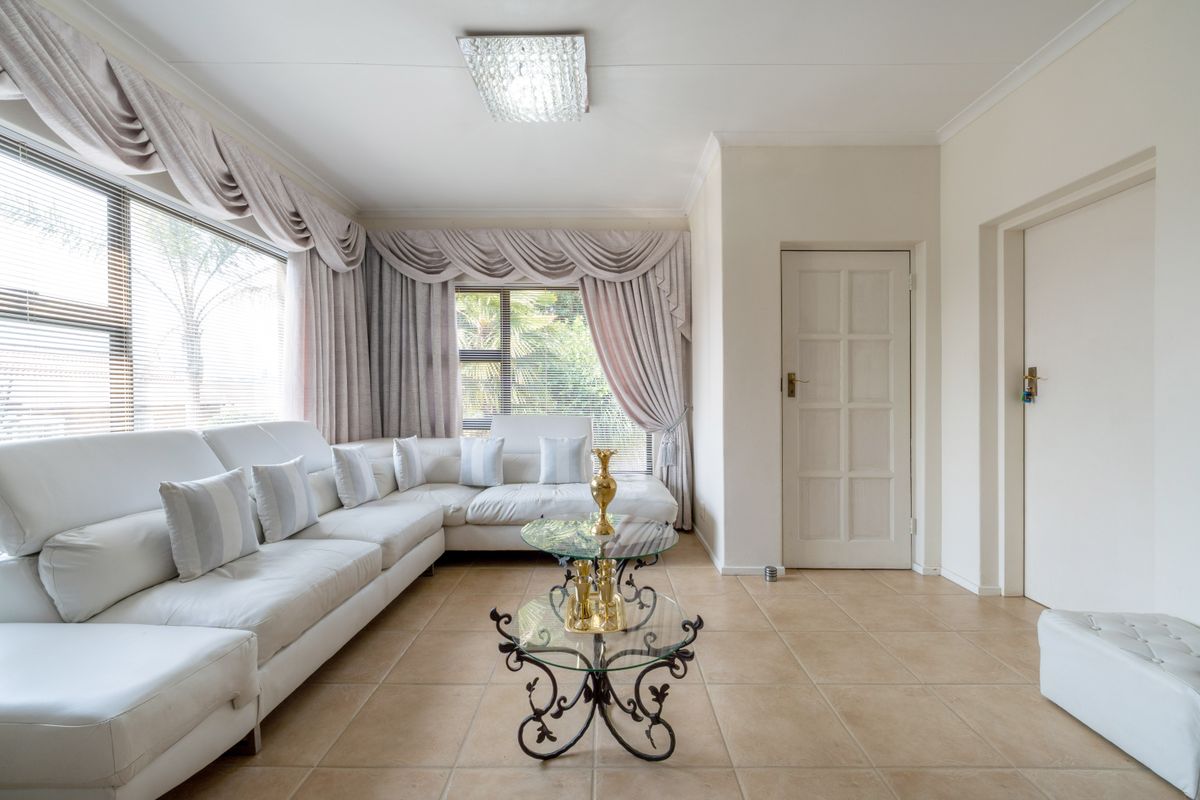 A bright living room featuring tiled flooring, coved cornicing, and large windows with integrated blinds, offering a neutral and functional living space.