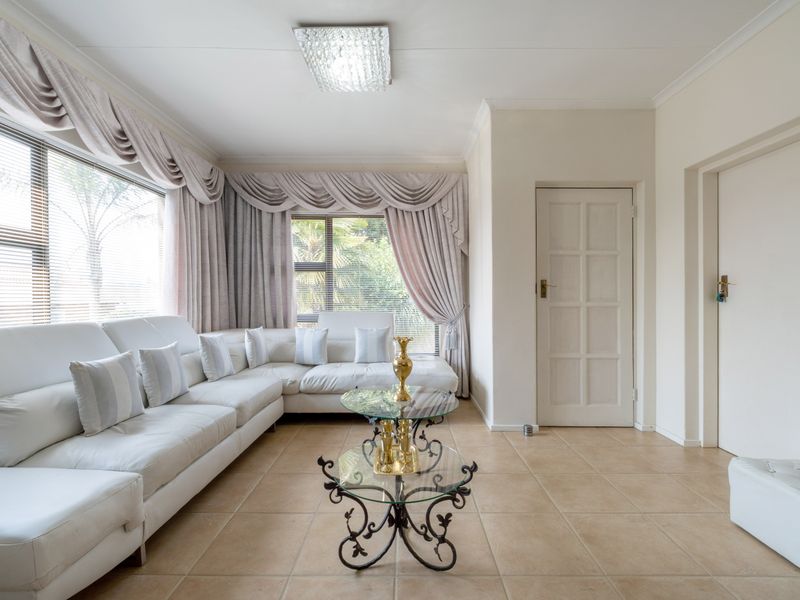 A bright living room featuring tiled flooring, coved cornicing, and large windows with integrated blinds, offering a neutral and functional living space.