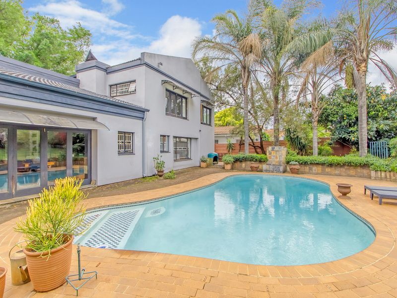 Rear exterior view featuring a swimming pool, paved deck area, stone water feature, and direct access to the home via sliding glass doors.