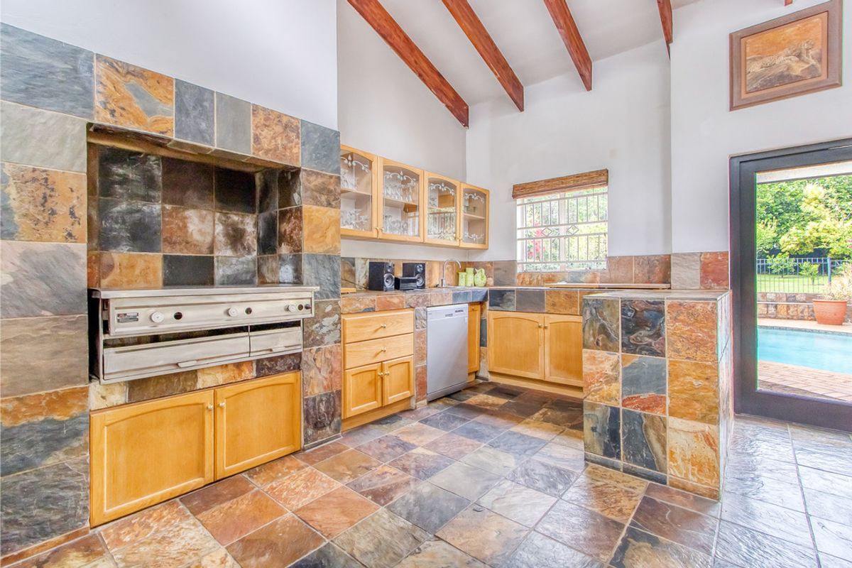 Kitchen featuring rustic slate tile finishes, exposed timber ceiling beams, built-in braai, and direct access to the outdoor pool area.