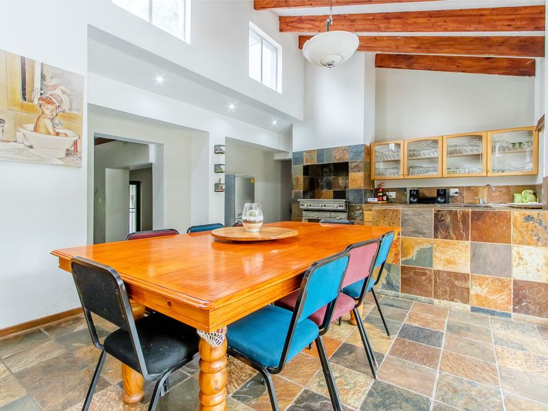 Open-plan living and dining area featuring exposed timber beams, slate tile flooring, and a rustic kitchen with slate backsplash and built-in cabinetry.
