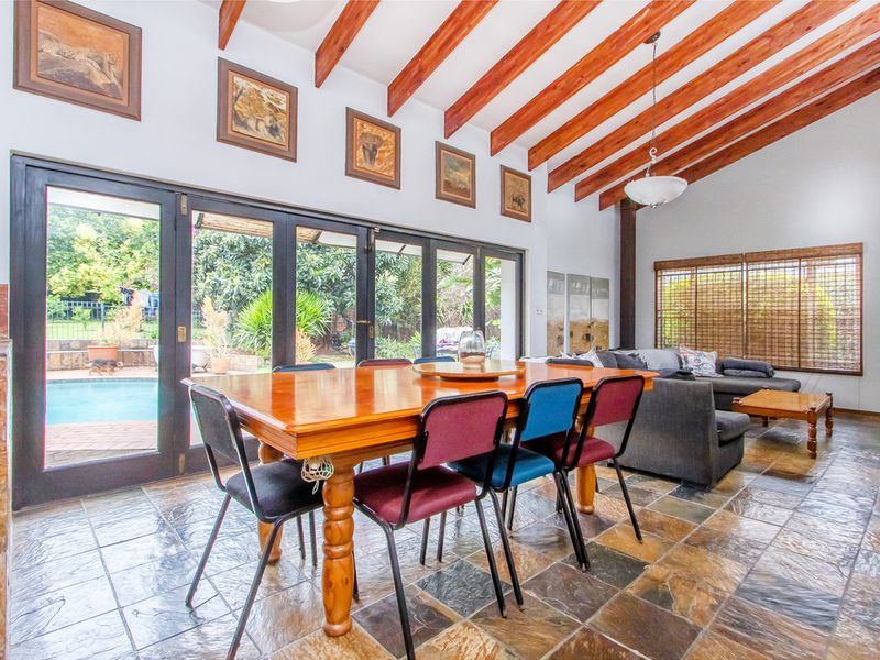 Spacious open-plan living and dining area featuring exposed timber beams, slate flooring, and large bi-fold doors opening to the pool area.