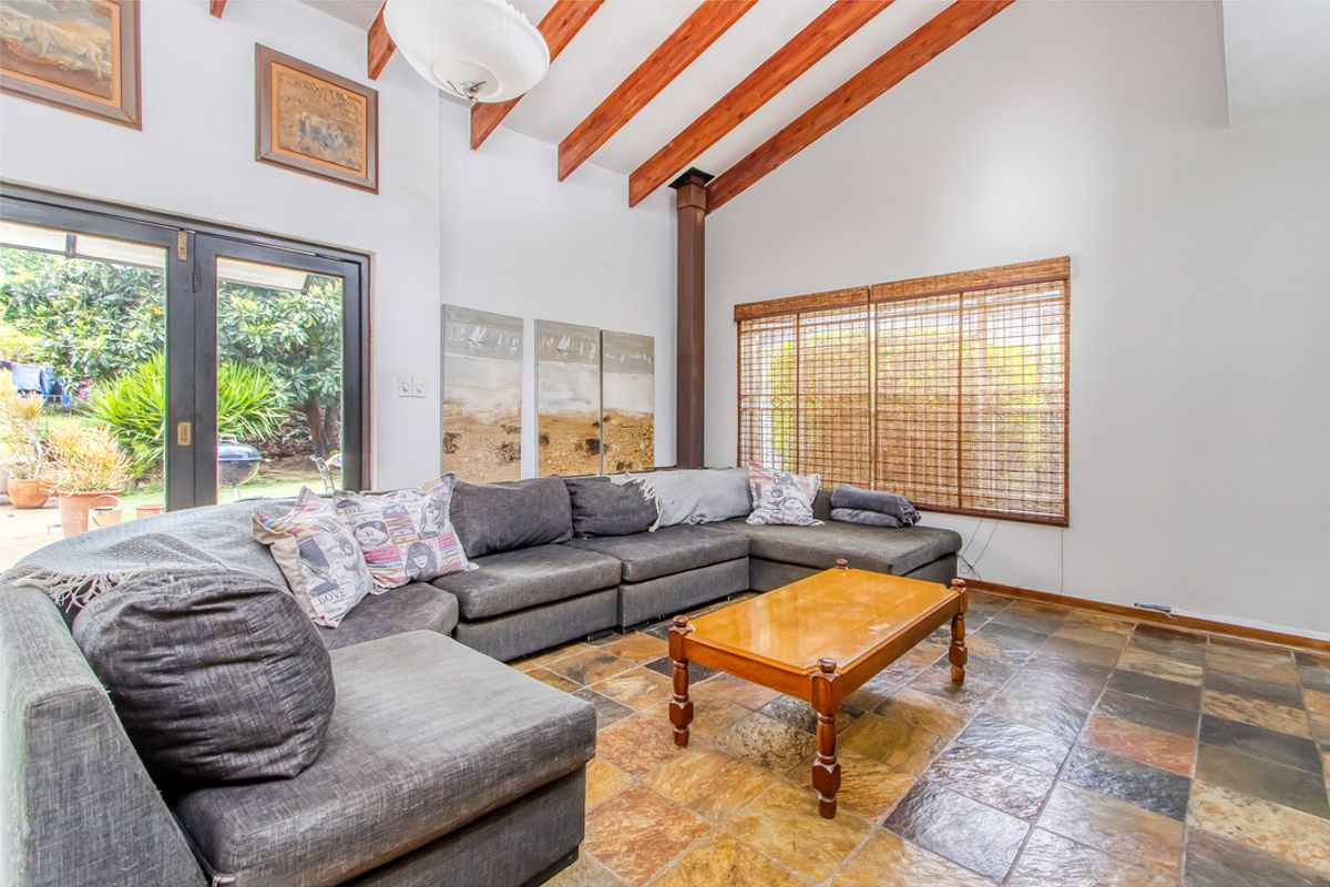 Spacious living room featuring high vaulted ceilings with exposed timber beams, slate tile flooring, and direct access to the garden through sliding glass doors.