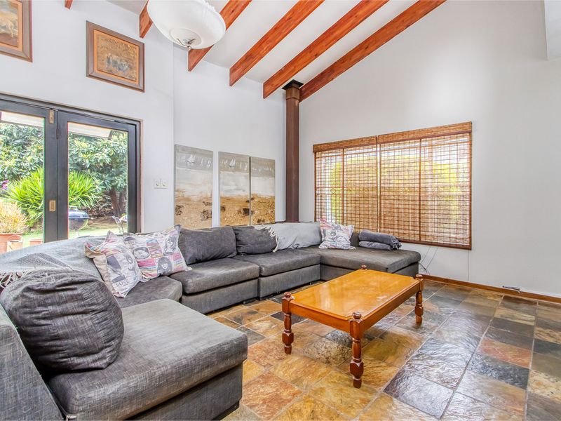 Spacious living room featuring high vaulted ceilings with exposed timber beams, slate tile flooring, and direct access to the garden through sliding glass doors.